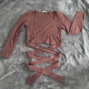 Ribbad omlott-tröja med knytband - Brun omlott-tröja med band som går att knyta på valfritt sätt runt midjan. Från ZARA, använd ett fåtal gånger. Kan skicka bilder med plagget på om så efterfrågas 🫶