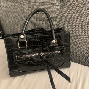 Svart väska  - Svart väska. Fake orm skinn och en dragkedja som detalj. Man får plats med mycket.