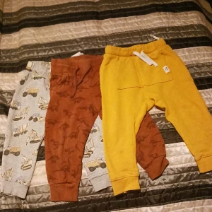 3 mjukisbyxor barn - Från vänster: 1 gråa med fordonsmotiv storlek: 92. 1 bruna med dinosariermotiv storlek: 92. 1 gula märke n.y c i storlek: 92. Använt skick.