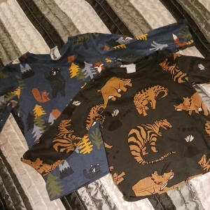 2 tröjor barn - 1 mörkblå med skogsdjur motiv i storlek 98. 1 mörkgrå/svart med dinosarier motiv i storlek 92, inköpta från Lindex, nyskick