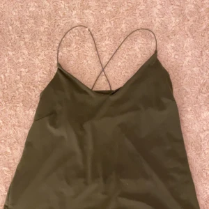 Grön silkes top - Banden är korsade i ryggen, super snyggt!! Mörk grön, materialet är silkes likt (är inte säker va det är för material). Jätte snygg!