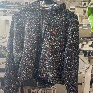 Hoodie från Levis - Svart hoodie med massa blommor i olika färger. Fint skick! Vid slutet finns så att man kan spänna in den.