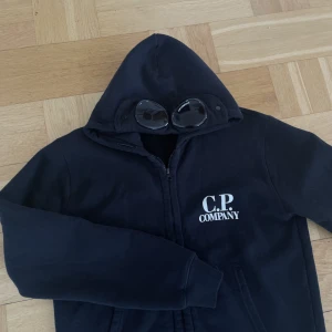 Hoodie från C.P Company - Svart C.P Company säljes pga använder inte längre. Mycket bra skick och köptes för runt 2500 kronor. Säljes för 750 inklusive frakt. Barnstorlek men motsvarar en S. Brukar ha XS (160cm lång) och den är en aning för stor för mig.