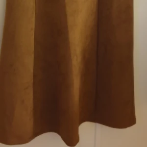 Knälång brunklänning storlek 48 - Säljer en fin brun klänning i storlek 48 men ganska flexibel i storleken. Den har guldiga dragkedjor och detaljer. Når till knät på mig som är 170 cm. Mycket fin och sparsamt använd. Inga deffekter ioch inget slitage.  