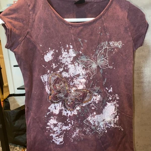 D&G T-shirt  - En lila lite ”urtvättad” i färgen snygg T-shirt med fjärils-tryck, paljetter och stenar. Den är storlek M men skulle verkligen säga mer S/XS. Snyggpassgprm och sömmarna som går i mitten av tröjan framhäver lite större byst.
