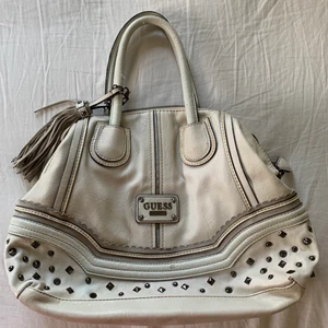 Vit GUESS väska - Guess väska med snygga detaljer och nitar🤍 Är väldigt rymlig och praktisk! Skick är enligt bild, framsidan är i bra skick men slitningar bak och på handtagen, pris diskuterbart 