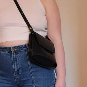 Mörkblå väska - Mörkblå axelremsväska med gulddetaljer. Har två innerfack, ett stort och ett litet, samt magnetlås. Axelremmen går att justera om man gör fler hål i den. I fint skick. Är ungefär 25x20 cm.