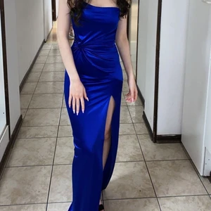 Blå långklänning satin från Fashion Nova - Den är i väldigt bra skick i bra kvalite o använd endast två ggr. Klänningen är i storlek XS men passar mer som XXS då den är tajt. Enaxlad med hög slits