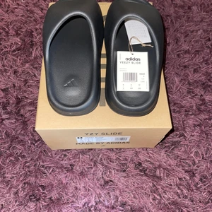 Adidas Yeezy slides  - Adidas Yeezy slides ”onyx”, vunna på adidas confirmed, dead stock alltså aldrig använda, storlek 42 och säljs för 1200 kr, pris kan annars diskuteras.