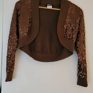 Bolero brun med paljetter - NY SKICK, den är köpt för ca 2 år sen och har bara legat i garderoben för att dem var inte min stil, så tröjan är som ny om du vill se fler bilder skriv privat. PRIS KAN DISKUTERAS den är perfekt att ha över en klänning eller till jeans.