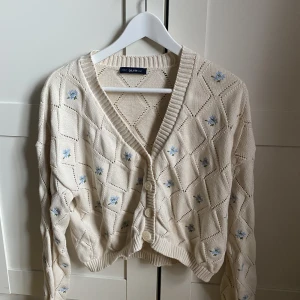 Stickad kofta  - En vit stickad kofta med blommor på från chiquelle! Väldigt sparsamt använd! 