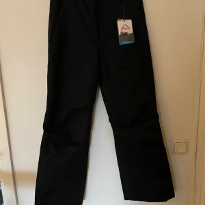 Helt oanvända svarta termobyxor/skidbyxor med avtagbara hängslen. storlek 164 - Vattentåliga, varma byxor perfekt för att vara ute på vintern eller åka skidor. Oanvända, nypris 499. 