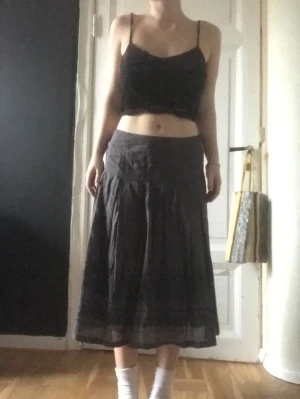Mörk kjol - Långkjol med mönster i kanten. En varm grå färg. Sitter tightare vid midjan och blir sen vidare. En 10 cm dragkedja på sidan. Mycket gott skick