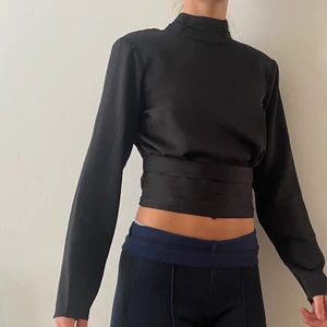 Silkestopp - Svart blus/topp i silkesliknande material. Knäpps med två knappar i nacken och en knut i ryggen.