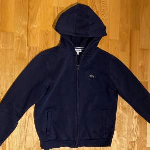 Säljer en navy zip hoodie från Lacoste. Den är i fint skick. Storlek 176cm motsvarar s/xs. Skicka dm för frågor eller fler bilder. Köparen står såklart för frakten.