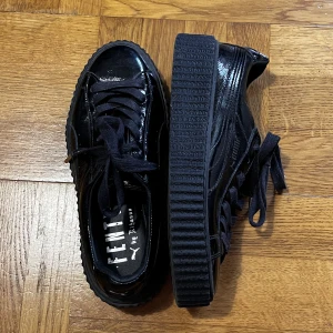 Fenty x Puma - Ett par svarta blanka sneakers från Rihannas Fenty kollektion med Puma! Säljer då dem är för små på mig som vanligtvis bär 38. Skulle säga att dem passar en större 36 eller 37 🖤De är i bra skick, endast använda vid 2 tillfällen!