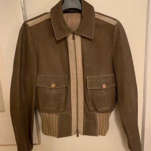 Läderjacka - Vintage läderjacka i äkta läder. Några tecken på användning syns, se sista bilden, men annars är den i väldigt bra skick. Lappen säger 40, men skulle snarare säga att det är en XS/liten S då den inte passar mig som är M i axlar. Skriv om fler biler!