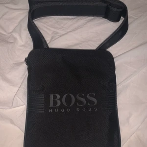 Hugo Boss axelväska - Använd men i nyskick och kan justera storlekar. Köpt för 1100 kr. Säljs inte längre i butik. För fler bilder kom dm. Möts upp i Årstaberg/Stockholm. Frakt funkar men kund står för det.