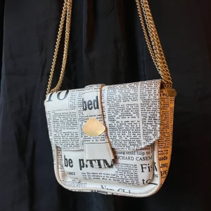 Axelväska med tidningsmönster - Handväska med trendigt tidningsmönster. Mått: ca 20cm x 23cm. Väskan är i bra skick trots att den är vintage. 