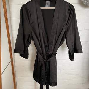 Vad: Svart kimono i sidenliknande material. Skärp och fin detalj på ryggen.  Storlek: XS (passar även S) Märke: 97% polyester 3% elastan  Skick: Utan anmärkning 