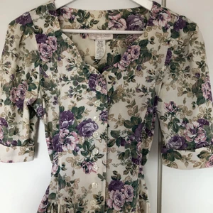 Blommig klänning - Helt fantastisk blommig vintageklänning i bomull. Knälång. Breda 80-tals axlar men jag har tagit ur axelvaddarna. Stängs med flera knappar fram. Det finns ett band i midjan som knyts bakåt för att markera midjan. På lappen står det ”size 5”, passar xs-s