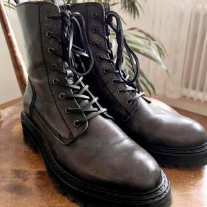 Svarta kängor från Billi Bi - Fina och rejäla vinterkängor från Billi Bi. De har snörning fram och dragkedja på skaftets insida. Material: 100% skinn. Klackhöjd: 3,9 cm. Originalpris: 2400kr. Skorna har använts ett fåtal gånger och har några små skavanker men inget som stör.