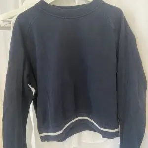 Marinblå sweatshirt med vita detaljer vid armarna också 