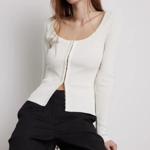 Tröja - Super fin tröja som är från Ida Carlssons kollektion med NA-KD. Denna cardigan är stickad och ribbad samt har en djup urringning. Den har en krokstängning i mitten av tröjan och i slutet av ärmarna. Använd 2 gånger så är i nyskick!