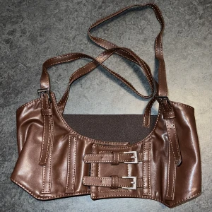 Korsett i brunt faux leather  - Strl S (midjemått 72cm), justerbar i storleken med kardborreband som stängning, kom aldrig till användning. Hör av er vid fler frågor!