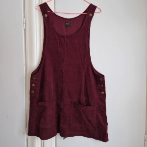 Manchesterklänning POP - Ljuvlig manchesterklänning från det retroinsoirerade märket POP (De har vintagebutik i Stockholm).  Djup vinröd färg. Kort längd. Fickor. Reglerbara hängslen med 2 olika lägen. Passar M/40-42