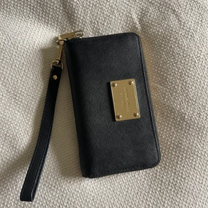 Michael Kors plånbok  - Svart plånbok från Michael Kors, guldiga deltaljer, svart handtag som går går att knäppa av, flera fack inuti, gott skick men repor finns på guldiga detaljerna! 