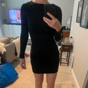 Svart klänning med gulddetaljer, strl XS - En svart klänning med tjockare material. Liten skurning längst ner baktill. Armarna har guldiga dragkedjor. 