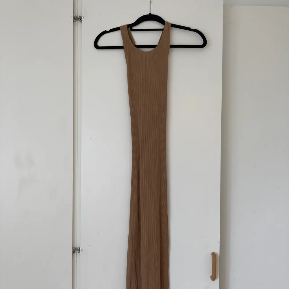 Lång brun klänning med öppen rygg, från NA-KD. Klänningen har två band som korsas och bildar en öppen rygg.. Klänningar.