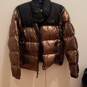 Guldig north face jacka  - Jag säljer min guldiga north face jacka eftersom att den inte längre kommer till användning. Den är knappt använd, och har inga tecken alls på användning. Den sitter lite oversized på mig som vanligtvis har storlek S i överdelar och jackor💙