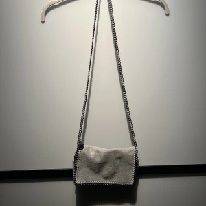 Stella McCartney väska - Grå skimrig väska från Stella McCartney i modellen ”Falabella shoulder bag”. Anpassningsbar- går att ha både crossbody & över axeln. Aldrig använd så inga defekter på väskan. Äkta & är köpt i Köpenhamn på Stella McCartney för några sedan! Nypris: 11 000kr