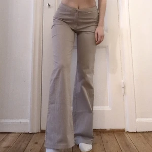 Kostymbyxor 90-tal - Supersnygga låg/mid waist kostymbyxor med utsvängda ben i grå-beige färg. Helt oanvända! Material: 97% bomull, 3% elastan. Mycket fin kvalitet!
