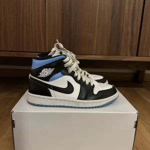 Air Jordan 1 - Säljer mina fina Mid Jordans i färgen white/black-university blue. Låda och kvitto finns.   Köparen står för frakt 
