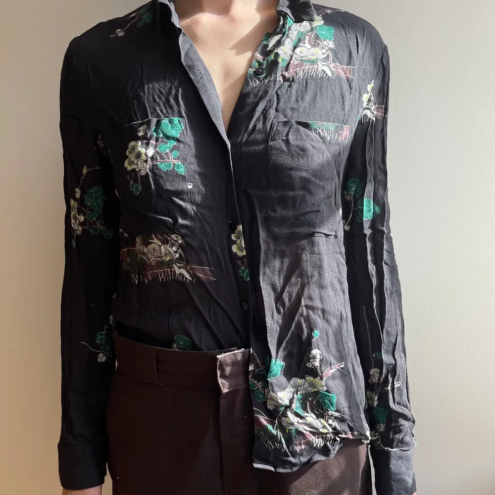 Svart blus i silke från Samsoe & Samsoe med blommönster i japansk stil. Plagget är i fint skick. Köptes för 2100Kr. Säljer vidare för 650Kr. . Skjortor.