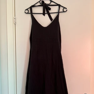 Svart tygklänning, öppen rygg  - En svart tygklänning med knytband runt nacken och öppen rygg. Perfekt till sommaren. Går ned till knäna på mig som är 163 cm lång. Säljer pga flytt och därmed utredning av garderob. 