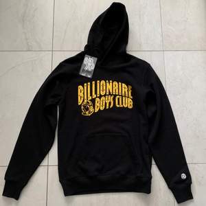 Säljer en oanvänd Billionaire boys club arch logo hoodie med lapparna kvar. Hoodien är i storlek S och har en glittrig/guldig logga. Hoodiens nypris är 2250kr. Säljer då den inte passar