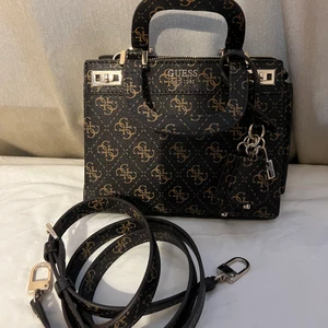 Guess väska  - Väska från guess. Aldrig använd på grund av att jag har andra väskor jag tycker om mer. Köpt för ca 1300kr. Helt ny. Band följer med så man kan välja om man vill ha den utan eller med. 
