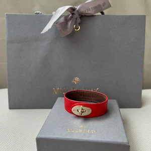 Mulberry Bayswater armband i korallrött  - L: 18,7cm & B: 2cm. Inga synliga repor på låset på utsidan. Lädret på insidan är färgat från användning, händer enl butiken vid kontakt med huden (bild). Köpt på Mulberry i London, kommer med kvitto, kartong och påse. Fler bilder kan skickas & kan postas!