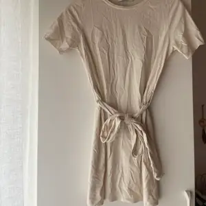 Gräddvit tshirt- klänning med knytningsdetalj.  Oanvänd.  Storlek: 36 Märke: NA-KD
