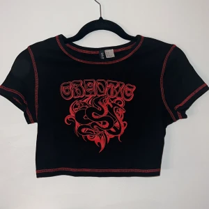 Croppad t-shirt med tryck - Tröja med rött tryck och röda sömmar. Storlek M men väldigt kort så jag skulle säga S/XS