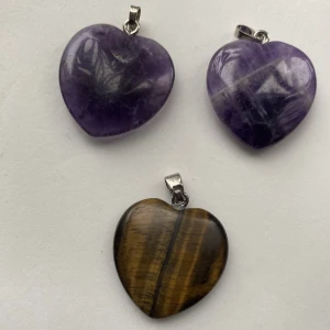 Kristall hänge - Säljer tre hjärtformade kristallhängen, den lila till vänster är ametist, den i mitten är tigeröga och den till höger är flourit. 1 för 40kr, 2 för 75kr 3 för 100kr