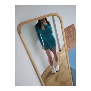 Klänning för utekvällen - Jättefin turkos klänning med urringning och twistad front som kan knytas. Slätt, slinky material. Tight modell, både längs kropp och armar. Går till mitten av låren ungefär. Helt oanvänd med lappen kvar.