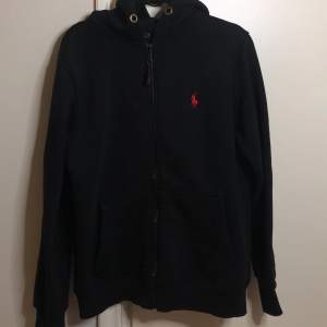 En Polo Ralph Lauren zip up hoodie i färgen svart, storlek S, saknar även band till huvan. Annars i bra skick, har använts ett par få gånger. 