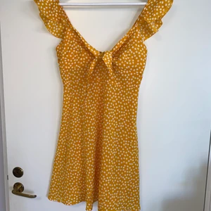 Klänning - Gul/orange klänning. Volang på axelbanden, knytning framtill och går lite över knäna på mig som är 160