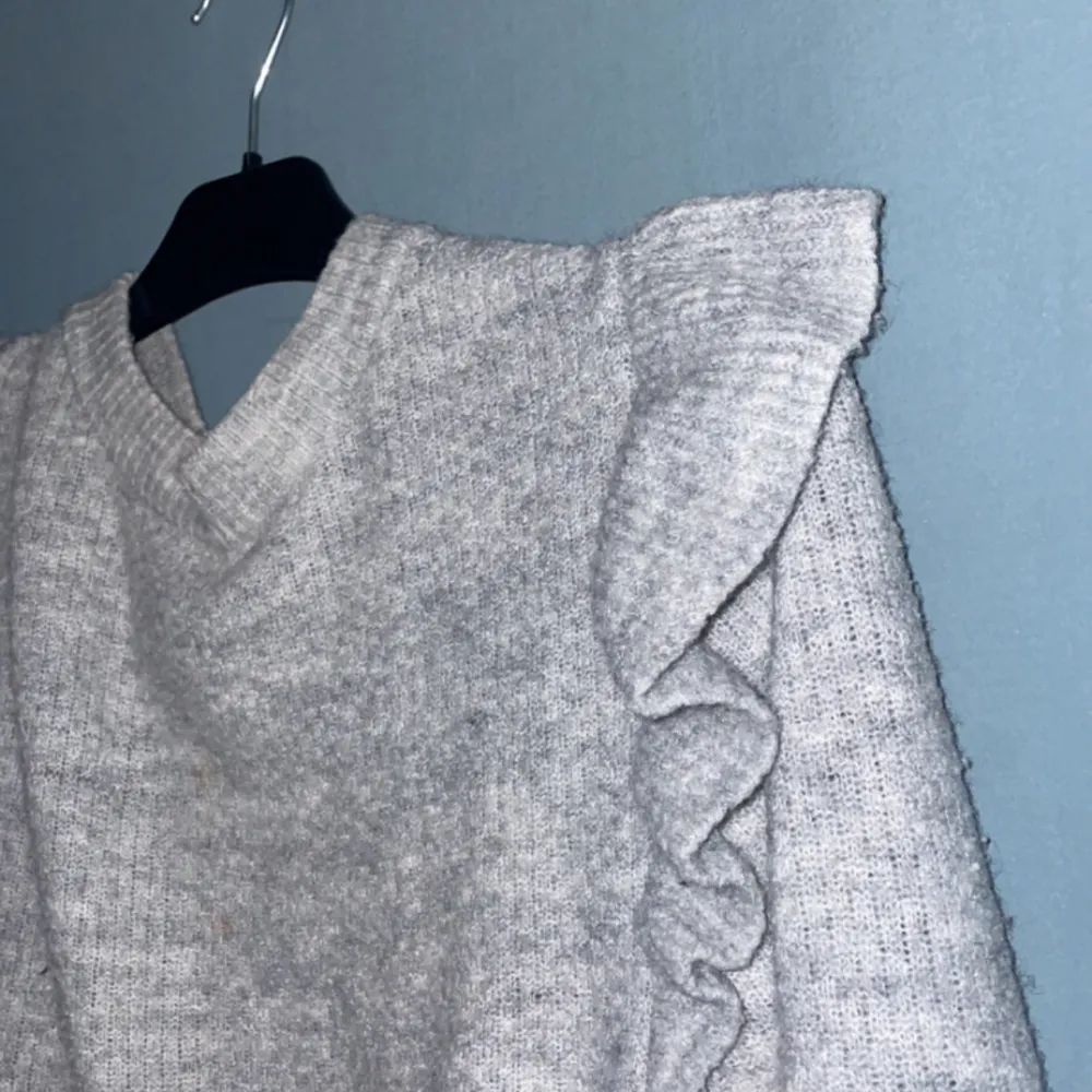 En grå stickad tröja från hm med en vulang på axlarna som även syns på baksidan Andvänd några gånger men fortfrande i fint skick  . Stickat.