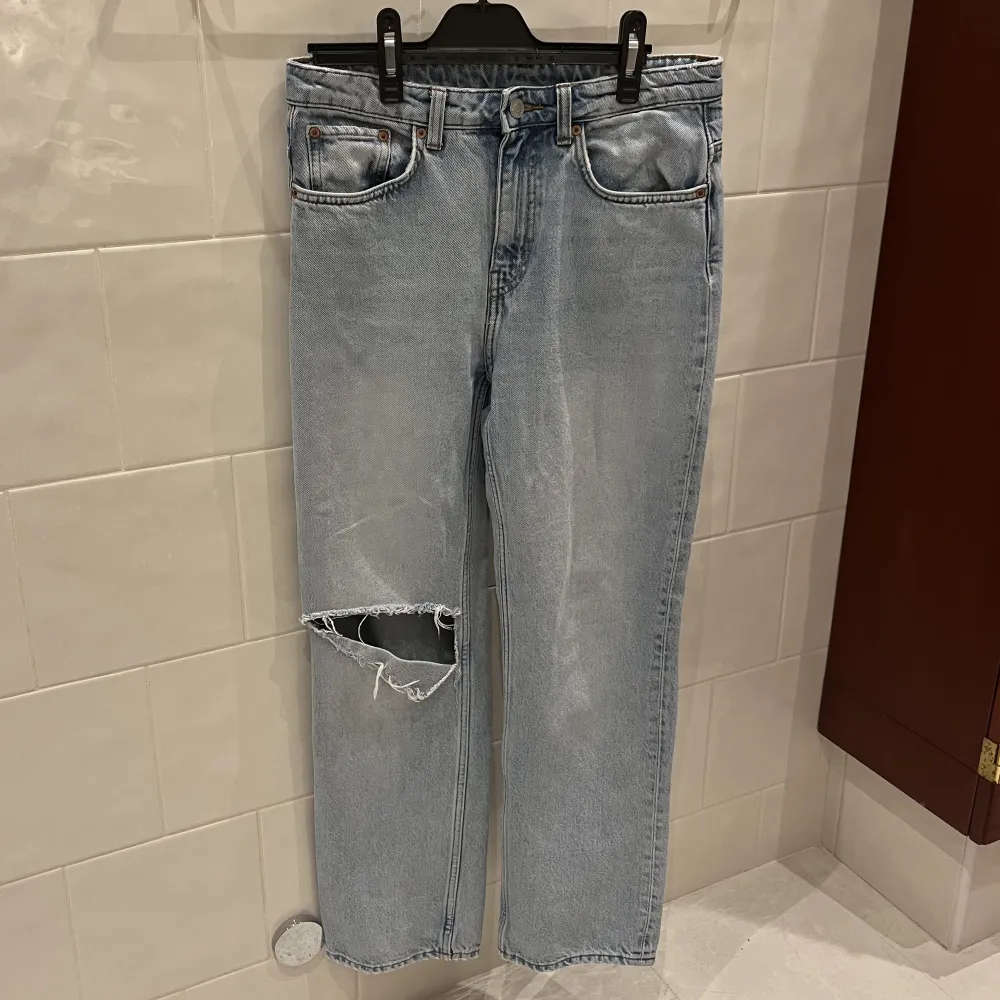 Straight jeans från Weekday i modellen VOYAGE. Superfin ljusblå urtvättad färg med ett egetklippt hål i knät som en fin detalj. Fint skick. Storlek 36. Skriv för fler bilder!. Jeans & Byxor.
